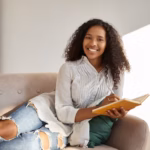 people-lifestyle-leisure-hobby-rest-adorable-charming-young-dark-skinned-woman-with-afro-hairdo-relaxing-comfortable-gray-couch-smiling-writing-down-goals-plans-diary_343059-4732